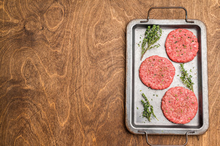 Raw hamburger minced meat patties for burgers with herbs on tray. wooden background. top viewの写真素材