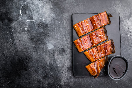 Unagi kabayaki eel, Japanese grilled fish fillet with sauce. black background. top view.