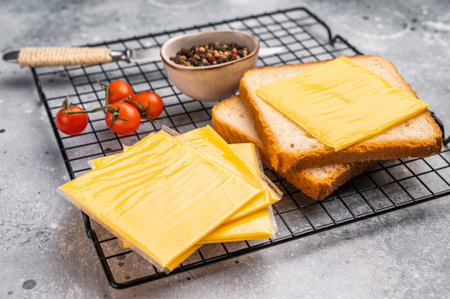 Square Slices of processed Cheddar cheese in individual plastic packaging. grey background. top view.の写真素材
