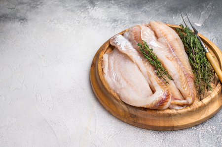 Fresh Raw Hake fish fillets, whitefish meat on a wooden board with herbs. white background. top view.の写真素材