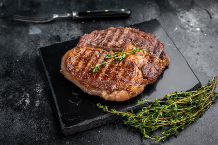 Rib eye steak with herbs on marble board, grilled prime beef meat. black background. top view.の写真素材