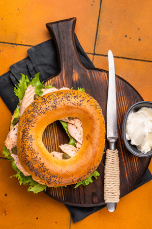 Breakfast Bagel with smoked salmon, lettuce and cream cheese on a wooden board. orange background. top view.の写真素材