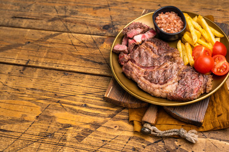A juicy Grilled Chuck eye roll steak and garnish with French fries on a plate. wooden background. top view.の写真素材
