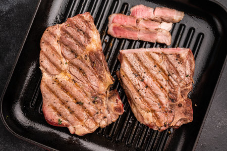 Fried on grill skillet pork tender steak, neck meat. black background. top view.