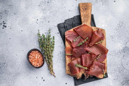 Dried beef meat Cecina, slices of beef jerky on wooden board with herbs. grey background. top view.の写真素材