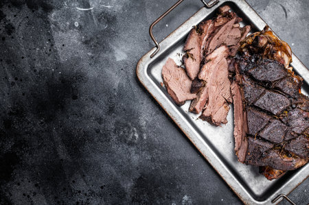 Roast Venison leg, baked meat of roe deer with bone on a tray with herbs. black background. top view.の写真素材
