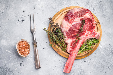 Uncooked tomahawk steak, raw black angus beef rib eye with bone on wooden board. gray background. top view.の写真素材
