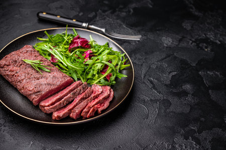 Grilled and sliced Flank beef steak on plate with salad. black background. top view.の写真素材