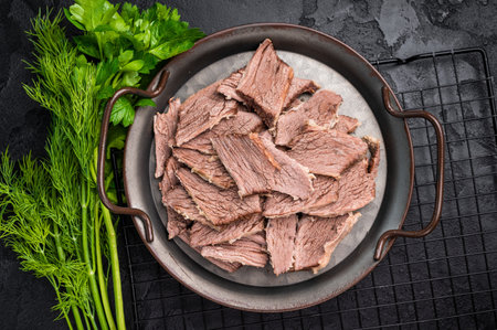 Boiled sliced beef meat in a steel tray. black background. top view.