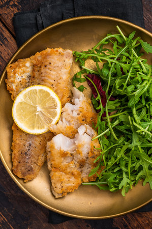 Roasted Pollock fish fillet on a plate with salad. wooden background. top view.