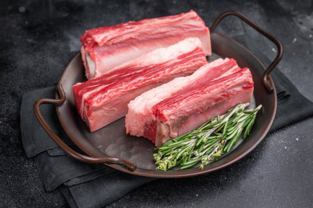 Raw bone-in beef short ribs ready for cooking, garnished with rosemary sprigs on a dark metal platter. Perfect for a recipe or menuの写真素材