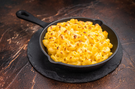 Baked mac and cheese in a black skillet, set against a rustic dark brown background.の写真素材