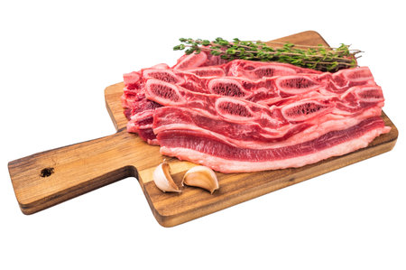Uncooked cross-cut beef short ribs ready for cooking, garnished with fresh herbs and garlic on a light backgroundの写真素材