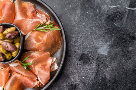 Appetizing dry cured ham Jamon and Kalamata olives served on a dark textured surface. Top viewの写真素材