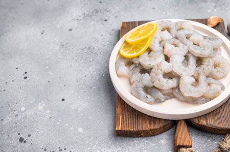 Fresh prawn shrimp tails on a wooden board. Gourmet ingredient with spices and lemon slices, ready for cooking on a rustic tableの写真素材