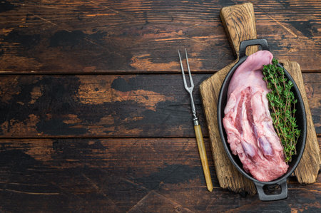 Fresh raw meat cut with thyme shown in skillet top view on rustic dark wood backdrop for slow cooking.の写真素材