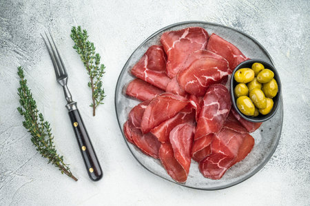 Gourmet Italian bresaola charcuterie with green olives and herbs, presented on a stone textured background for elegant flat layの写真素材