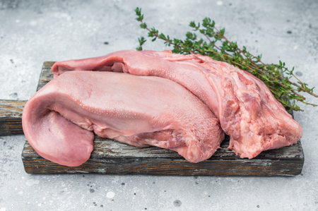 Whole uncooked lamb tongue displayed with herbs spices and vintage fork on light stone background perfect for cuisine prep and food photography.の写真素材