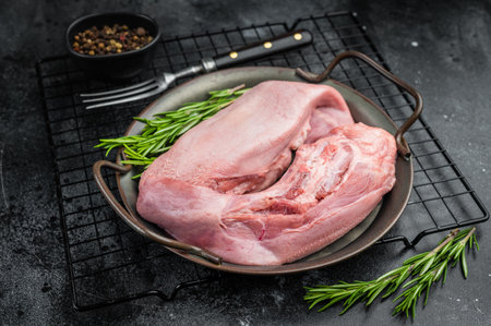 Whole raw uncooked pork tongue offal in skillet with herbs and vintage fork top view on dark background.の写真素材