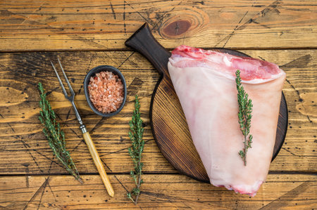 Raw pork knuckle hock with rind bone and muscle fibers on rustic board with thyme salt and meat fork ideal for butchery prep and culinary detailingの写真素材