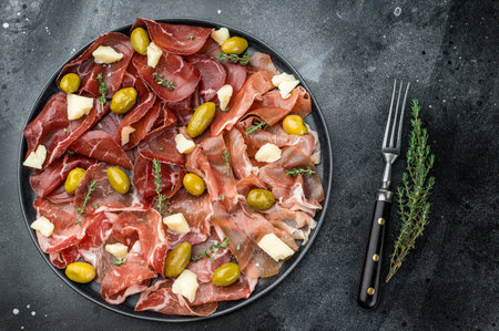 Italian charcuterie platter with bresaola, prosciutto, coppa, olives and parmesan on a dark textured background with copy spaceの写真素材