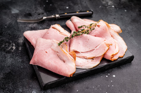 Sliced smoked ham on black slate board with knife and forkの写真素材