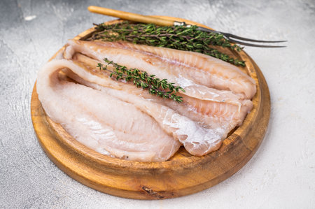 Fresh Raw Hake fish fillets, whitefish meat on a wooden board with herbs. white background. top view.の写真素材