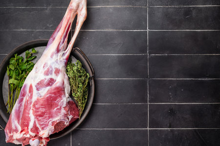 Uncooked whole lamb leg, raw mutton meat with herbs for cooking. black background. top view.の写真素材