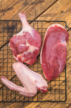 Fresh uncooked duck cuts breast fillet thigh and wingarranged on cooling grid against scratched wood surface perfect for culinary preparation visualsの写真素材