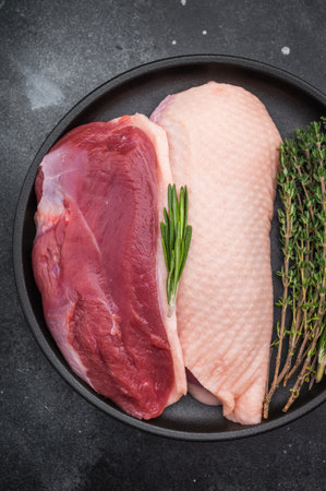 Raw duck breasts skin on and skinless with rosemary and thyme in black plate on dark stone background ideal for gourmet poultry stock imagesの写真素材
