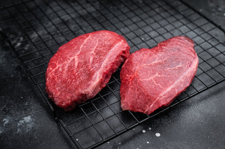 Marbled Wagyu beef chuck steaks similar to angus and yakiniku cuts placed on grill rack with pepper bowl on dark stone backdrop great for butcher photographyの写真素材