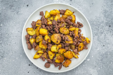 Crispy fried potatoes with ground beef served on a white plate, hearty homemade hash on a rustic grey backgroundの写真素材