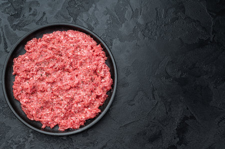 Fresh raw ground mince beef and pork meat with seasoning on black plate over dark textured background.の写真素材