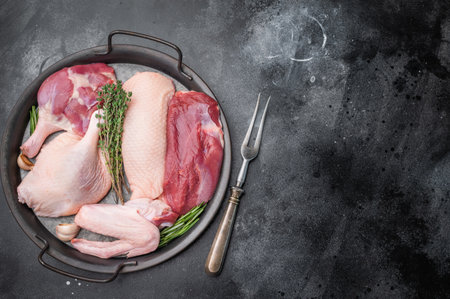 Fresh uncooked duck assortment arranged with thyme rosemary and garlic in rustic pan against textured dark surface perfect for culinary visualsの写真素材