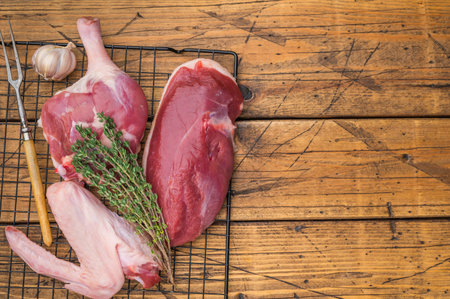 Fresh uncooked duck cuts breast fillet thigh and wing arranged on cooling grid against scratched wood surface perfect for culinary preparation visualsの写真素材