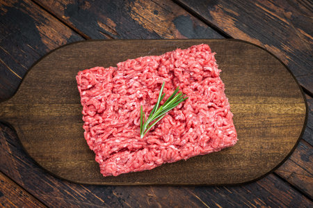 Fresh raw groundmeat with rosemary and thyme on dark wooden board over rustic table ideal for...