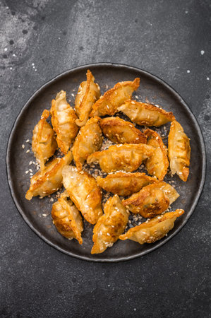 Crunchy gyoza wonton dumplings on dark stone background savory Asian dish with golden crust and sesame garnish.の写真素材