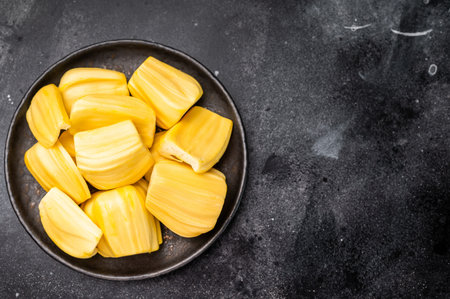 Sweet, golden yellow jackfruit pods (bulbs) served in a black plate on a dark stone background....