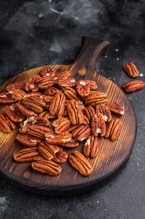 Raw pecan halves spread on a rustic wooden board placed on a dark textured background creating a...