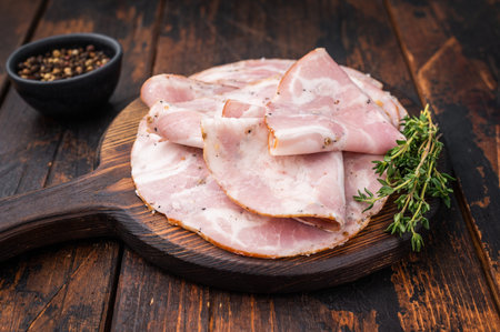 Slices of authentic Italian Pancetta Arrotolata served on a dark rustic cutting board with fresh...