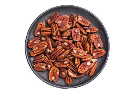 Shelled pecan halves spread on a dark plate over a bright white background creating a clean...