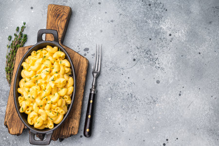 Creamy mac and cheese in a black cast iron skillet, resting on a rustic wooden board against a gray...