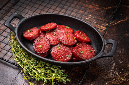 Fried Turkish sucuk (sujuk) slices in a cast iron pan with thyme and spices on a dark rustic wooden tableの写真素材