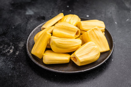 Sweet, golden yellow jackfruit pods (bulbs) served in a black plate on a dark stone background....