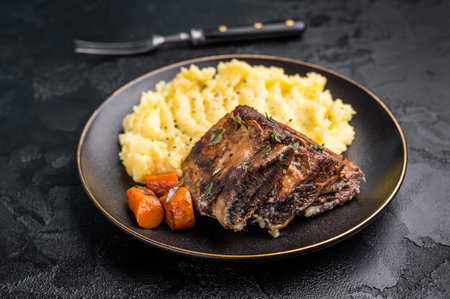 Braised beef short ribs resting on a bed of creamy mashed potatoes, creating an inviting culinary scene. black background. top view.の写真素材