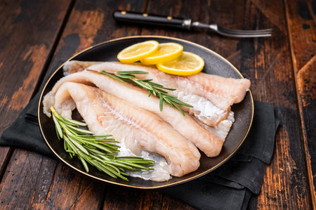 Organic Raw Haddock fish fillets, whitefish on a plate with herbs. wooden background. top view.
