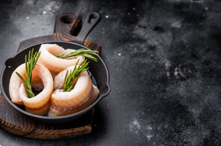 Ready for cooking Raw Pollock fish fillets in pan with herbs. black background. top view.