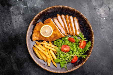 Roast viennese schnitzel steak, breaded meat with salad and french fry on a plate. black background....
