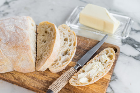 Sliced ciabatta bread with fresh butter on a wooden cutting board. marble background. top view.