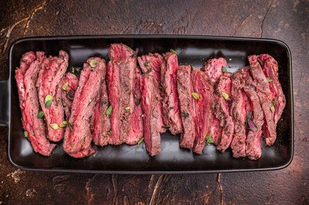 BBQ Grilled Flank beef steak, sliced meat with herbs, brown background. top view.の写真素材